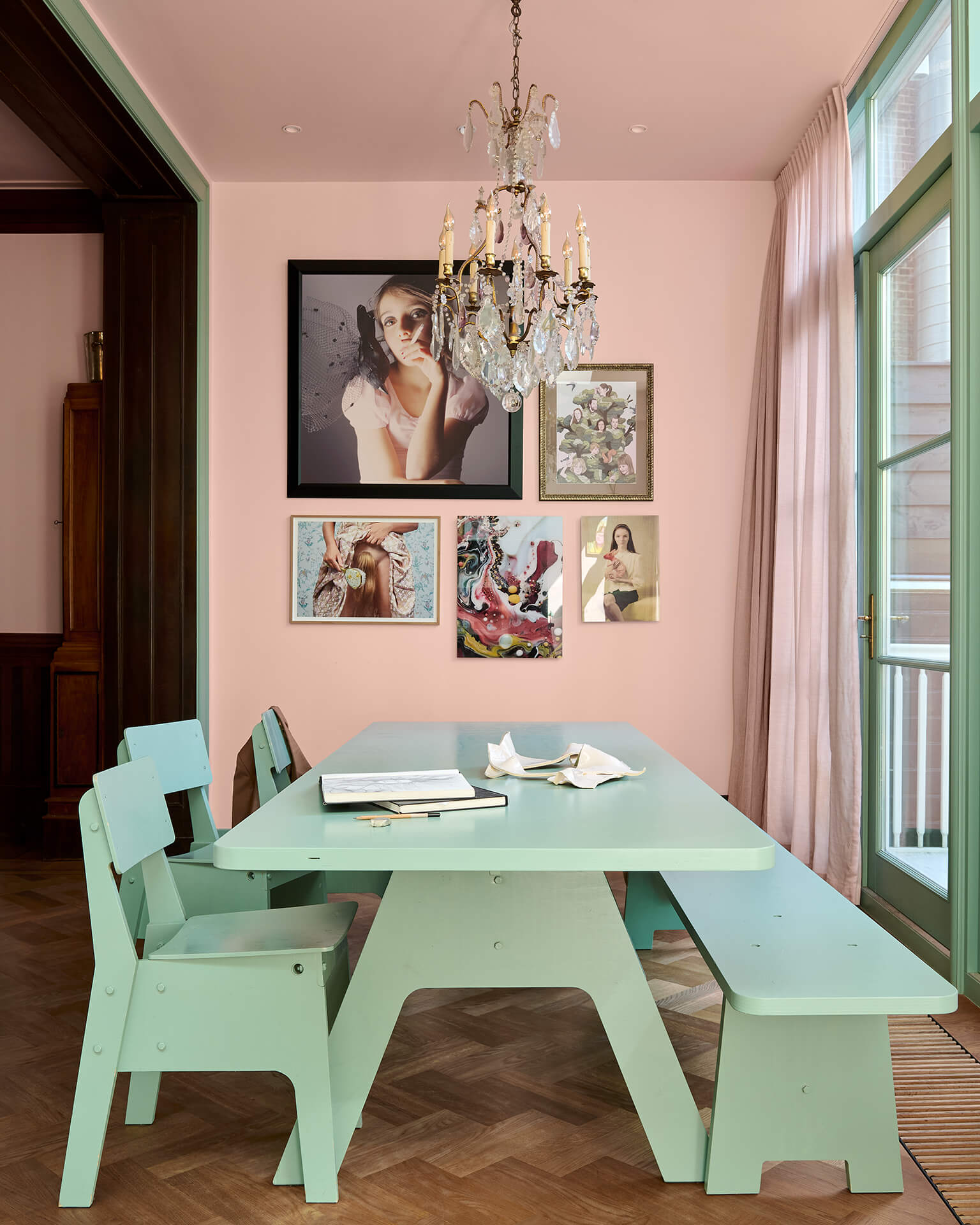 Pink dining room with a mint green table and benches and a gallery wall of artworks