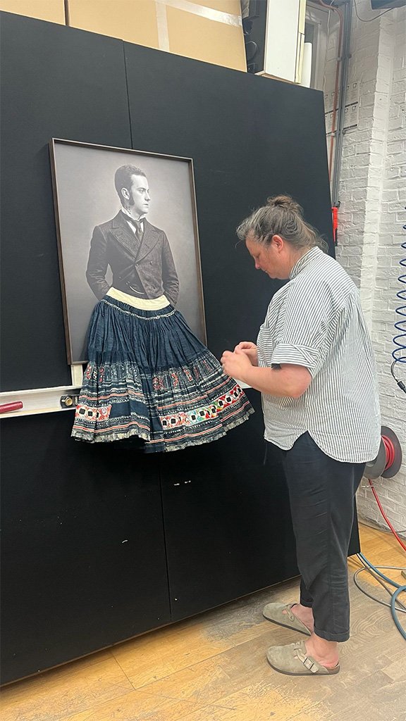 Artist hanging an embroidered skirt below a framed portrait